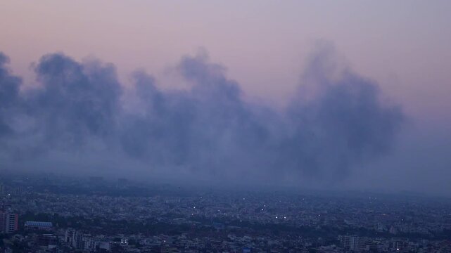 Dark smoke over Jaipur city at sunset seen from Nahargarh Fort, wide skyline with dense buildings, dramatic sky with smoke clouds and distant Aravalli hills.