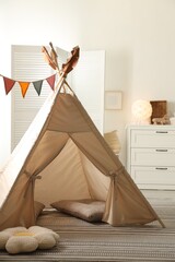 Stylish toy wigwam, furniture, pillows and decor in light playroom. Interior design © New Africa