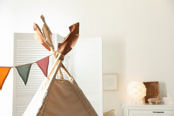 Stylish toy wigwam with colorful flags in playroom, closeup with space for text. Interior design © New Africa