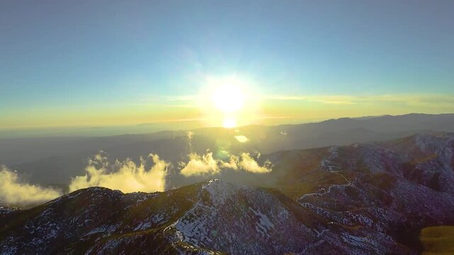 Late afternoon aerial view looking into the setting sun and backlit broken clouds over the snow-capped mountains of Southern California's Los Padres National Forest.