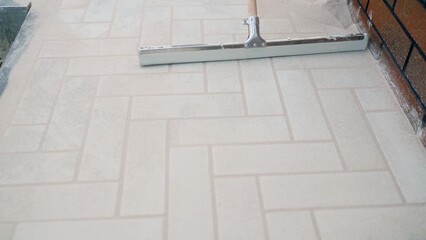 Spreading polymeric sand into joints of new outdoor herringbone paver patio.