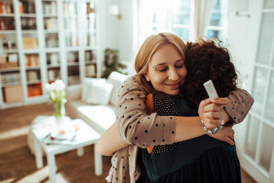 Two women hugging with positive pregnancy test at home