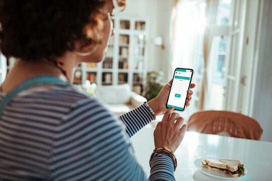 Young woman using telemedicine app on smartphone at home kitchen table