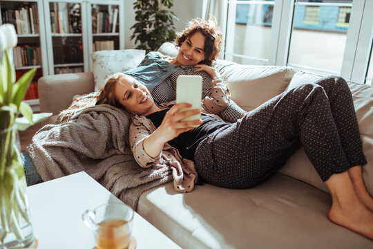 Two friends taking selfie while relaxing on sofa at home