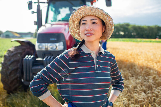Confident woman farmer by tractor in wheat field