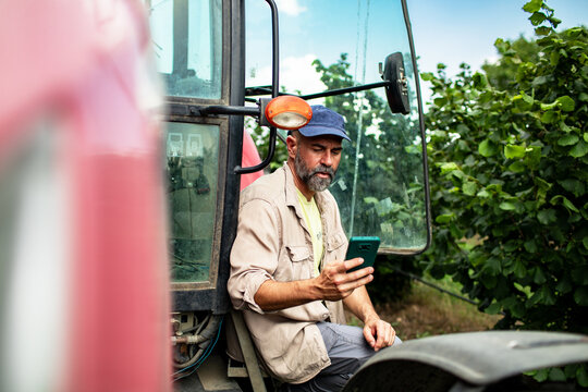 Farmer using smartphone on tractor in orchard