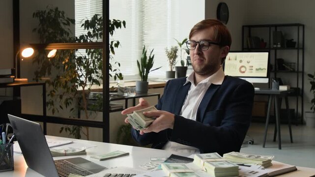 Successful gen Z male manager counting dollar banknotes and looking at them with excitement at workplace