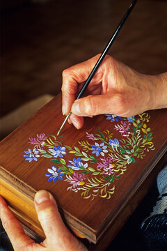 Artisan paints flowers on wooden box in Les Jouets du Queyras regional natural park in France