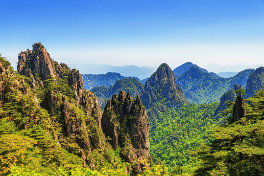 Bijia Peak is viewed from a distance, highlighting its distinctive shape amid surrounding green hills and rocky mountains under a clear blue sky
