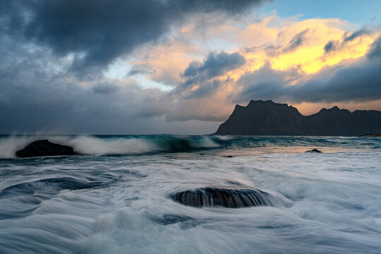 Waves crash on rocks along the rough sea at Uttakleiv beach during sunset in Norway&acirc;&euro;&trade;s Lofoten Islands