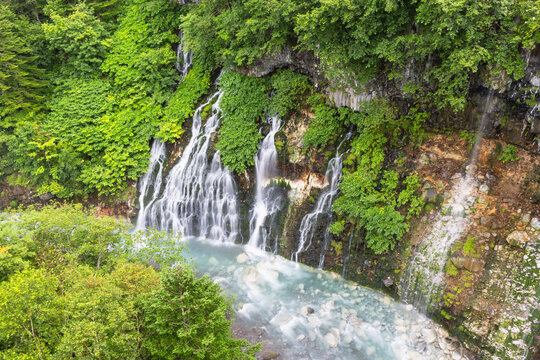 Shirahige waterfall flows through green trees in Biei, Hokkaido, Japan during summer