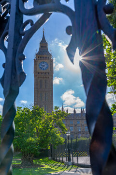 View of Big Ben clock tower with sunlight shining through trees in summer at Parliament Square, London, England, United Kingdom