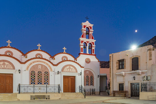 View of Church of the Metamorphosis of the Savior in Piskopiano village at dusk with warm lights and moon overhead