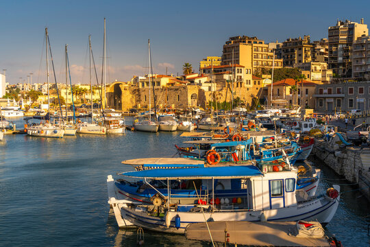 Boats docked at Heraklion Venetian Port during sunset in Crete, Greece, with buildings in the background