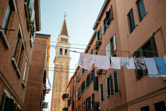 Washing hangs on clotheslines against bell tower in Castello area of Venice on a sunny day