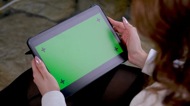 Close up of female hands holding a tablet with green screen chroma key markers for digital content viewing or mobile app demonstration outdoors during a peaceful day at home