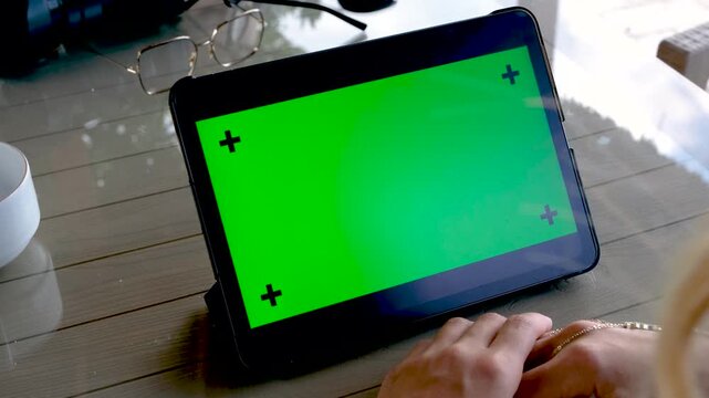 Close up of a woman hands holding and using a digital tablet with green screen chroma key in horizontal orientation while sitting on a sofa in a modern bright living room
