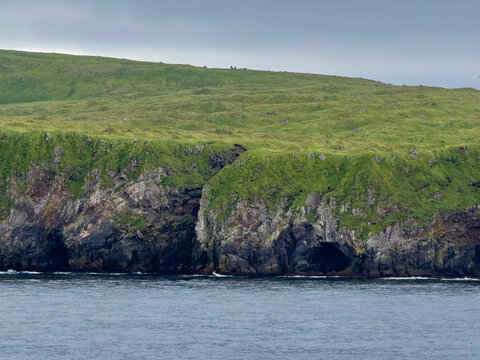 Rocky cliffs jut out above the water on Kagamil Island in the Aleutian Archipelago of Alaska during a cloudy day