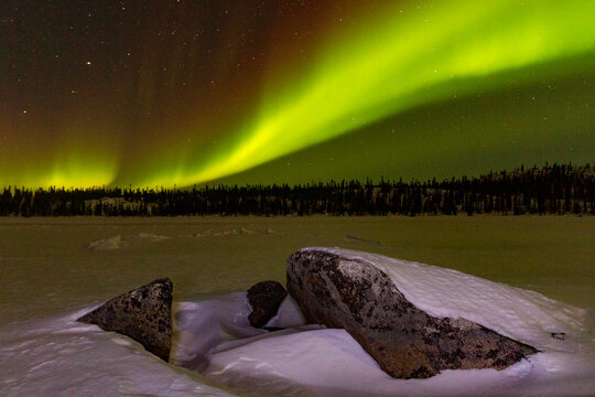 Aurora Borealis lights up the night sky over a frozen lake in boreal forest