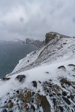 Snow covers ash and mud slides at Deception Island in Antarctica, showcasing the rugged coast and the Southern Ocean