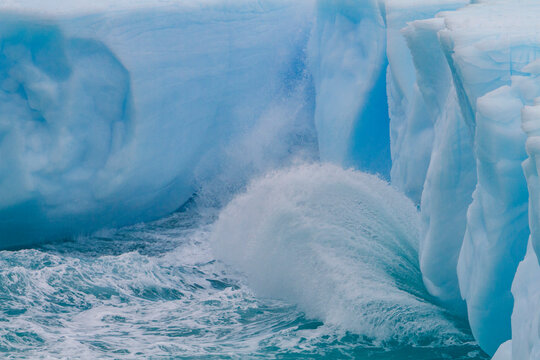 Iceberg detail shows blue tones in water with waves during Austral summer near Antarctic Peninsula