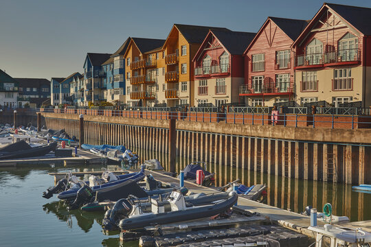 Evening sunlight shines on apartment buildings by the harbor in Exmouth, Devon, with boats moored in the still water