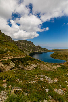 Views of Kidney Lake in Rila Mountains feature rocky slopes and grassy hills on a sunny day