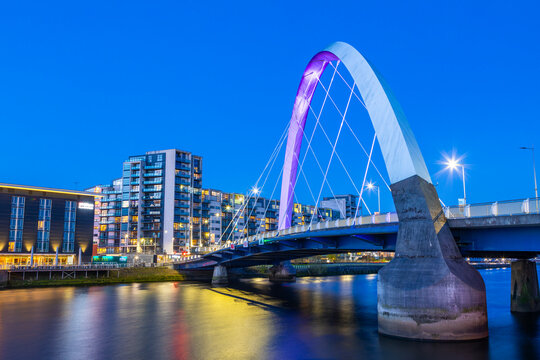 Clyde Arc bridge spans River Clyde at night in Glasgow, showcasing city lights and reflections on water