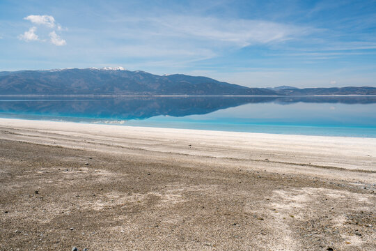 Salda Lake displays turquoise waters and white sand with mountains in the background during sunset in Turkey