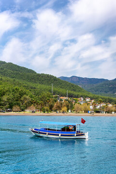 Tourist boat sails through the turquoise water of Ekincik in Turkey with hills and a small town in the background