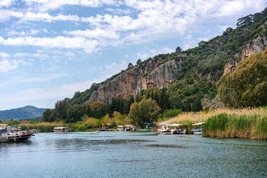 Tourist boats navigate Dalyan bay while ancient tombs sit on the hills in Turkey