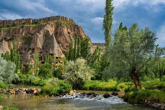 Selime houses sit by a river in Ihlara valley surrounded by trees and cliffs in Cappadocia Turkey