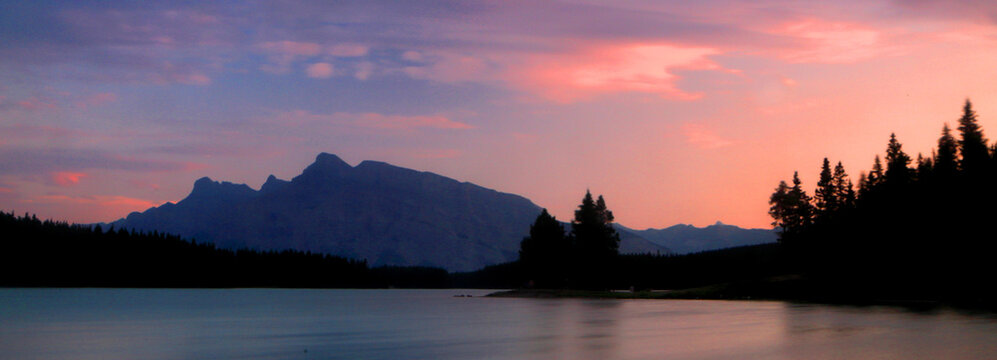 Sunset over Jack Lake and Rocky Mountains with trees visible along the shoreline near Banff, Alberta, Canada