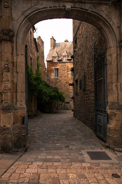 Historic stone archway leads to cobbled street with medieval houses in Dinan, Brittany, France