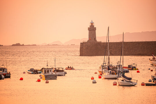 Fishing boats and Castle Breakwater Lighthouse at sunrise on the harbor in St Peter Port Guernsey Channel Islands