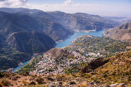 View of Guejar Sierra village alongside the blue Guenja Embalse lake at the foot of the Sierra Nevada in Spain