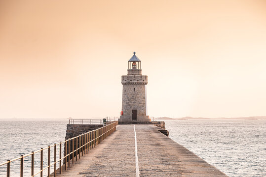 View of Saint Peter Port Lighthouse at sunset over the pier in Guernsey Channel Islands with stone pathway leading into the horizon