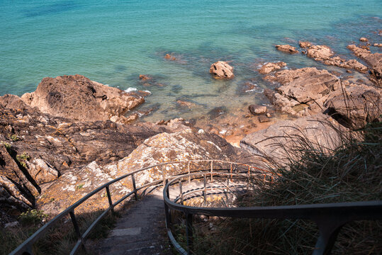 Stone staircase leads down to a rocky shoreline and water in Brittany, France during sunny weather