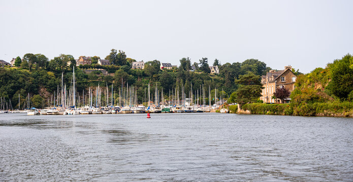Sailboats and yachts docked at a harbor in Dinan on the Rance estuary near green hills and traditional houses in Brittany, France