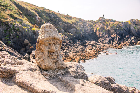 Sculpted stone face overlooks sea on rocky coast near Saint Malo in Brittany France during sunny weather