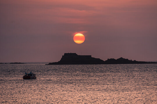 Golden-red sky at dusk over English Channel with Fort National and small boats in Saint Malo, France