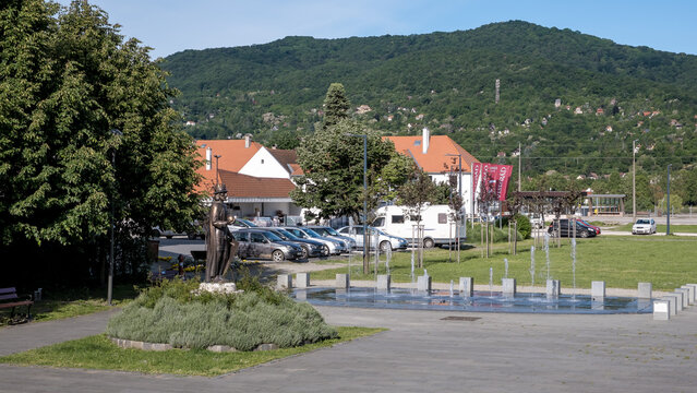 View of Visegrad park with benches, statue, and houses by forested hills in Danube Bend area
