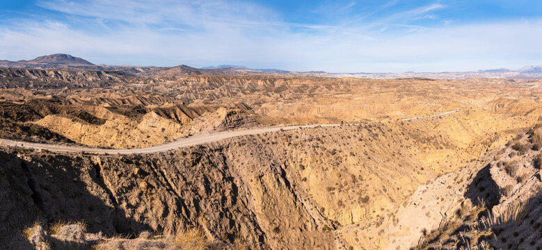 Rugged desert landscape with dirt road in Gorafe, Granada, Spain, showing vast terrain and geological features