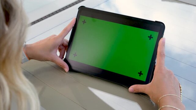 Side view of people using a tablet with green screen chroma key markers while sitting at an outdoor table for digital marketing or application mockup demonstration indoors at daytime