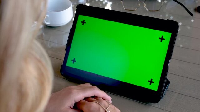 Hands of a person holding a digital tablet with blue screen chroma key for video editing or application interface mockup demonstration while sitting at a table indoors during day