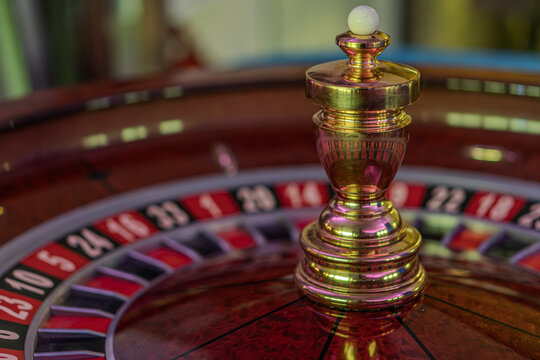 Close-up of a spinning roulette wheel in a blurred casino interior, featuring alternating red and black slots with numbers from 0 to 36, including two green zeroes A stationary white ball indicates