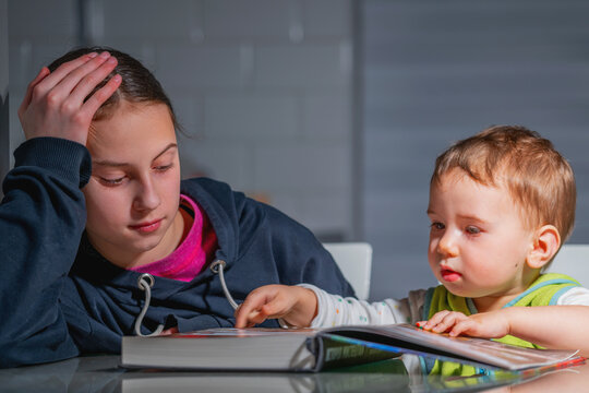 Unposed candid image of children with a book, showing genuine emotions, natural interaction, and authentic learning moment in a home setting.