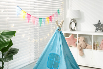 Toy wigwam, toys on shelving unit, colorful flags and decorative lights in child's room, closeup © New Africa