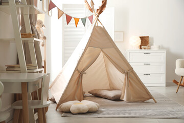 Stylish toy wigwam, furniture, pillows and decor in light playroom. Interior design © New Africa