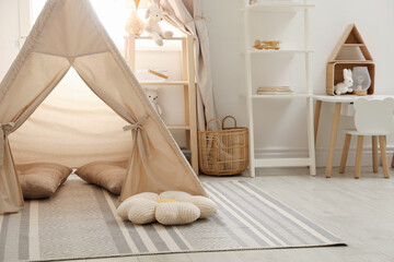 Stylish toy wigwam, furniture, pillows and decor near window in playroom. Interior design © New Africa